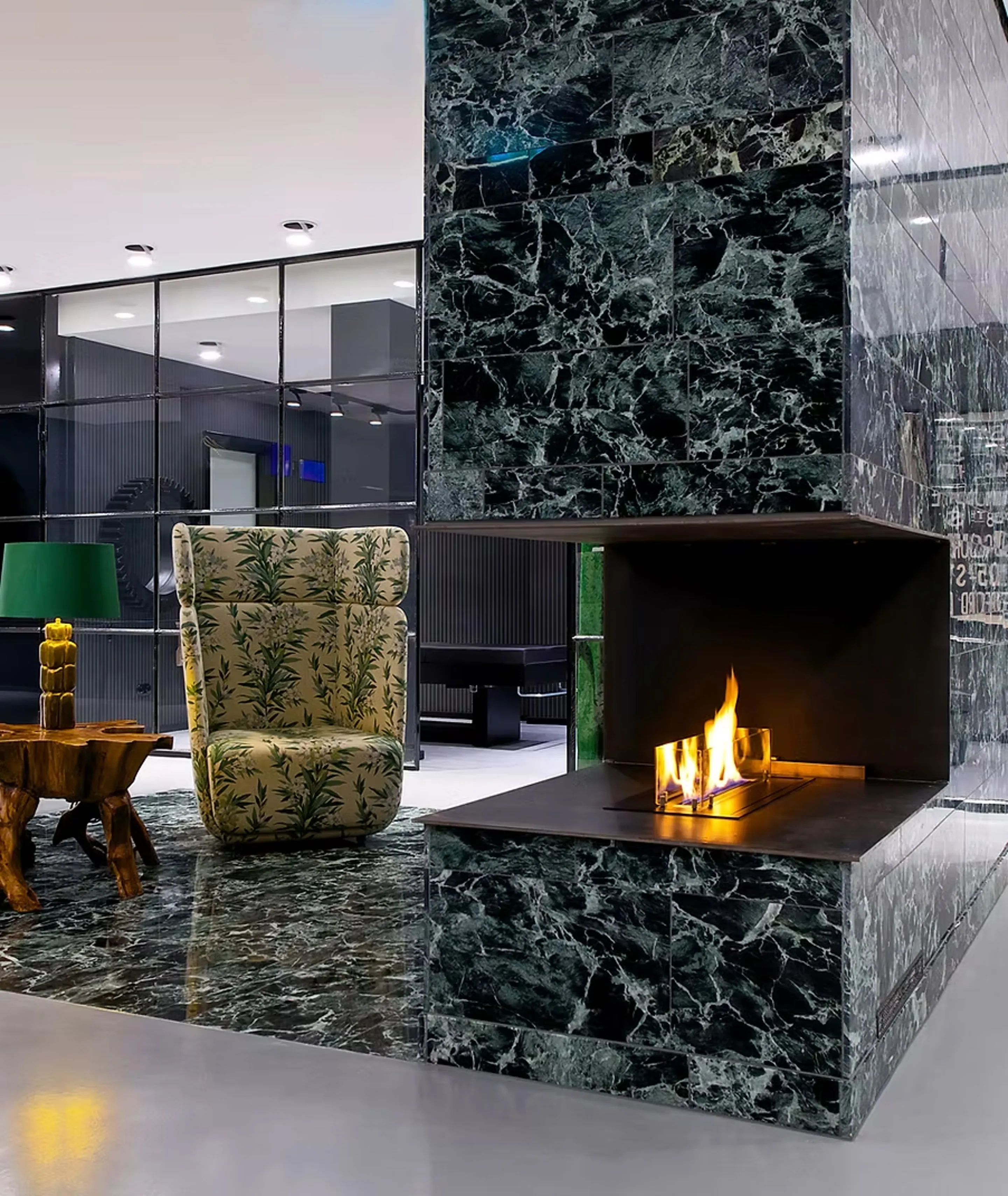 Lounge im Salon Königsallee: Ethanol-Kamin in grün marmorierter Wand, geblümter Ohrensessel und Wurzelholz-Beistelltisch