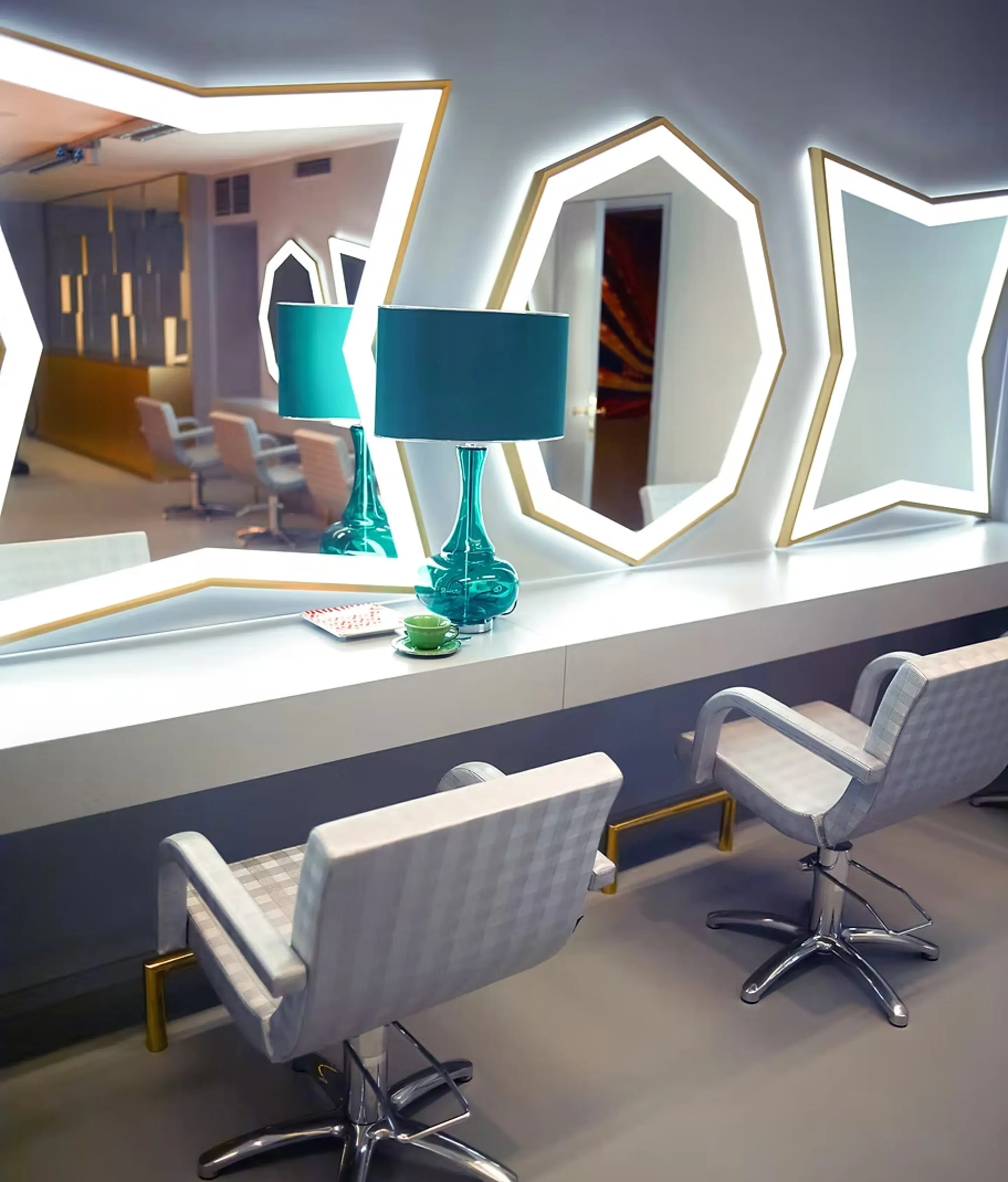 Stylingplätze im Salon Waitzstraße mit beleuchteten geometrischen Spiegeln, hellgrauen Stylingstühlen und türkisfarbener Tischlampe