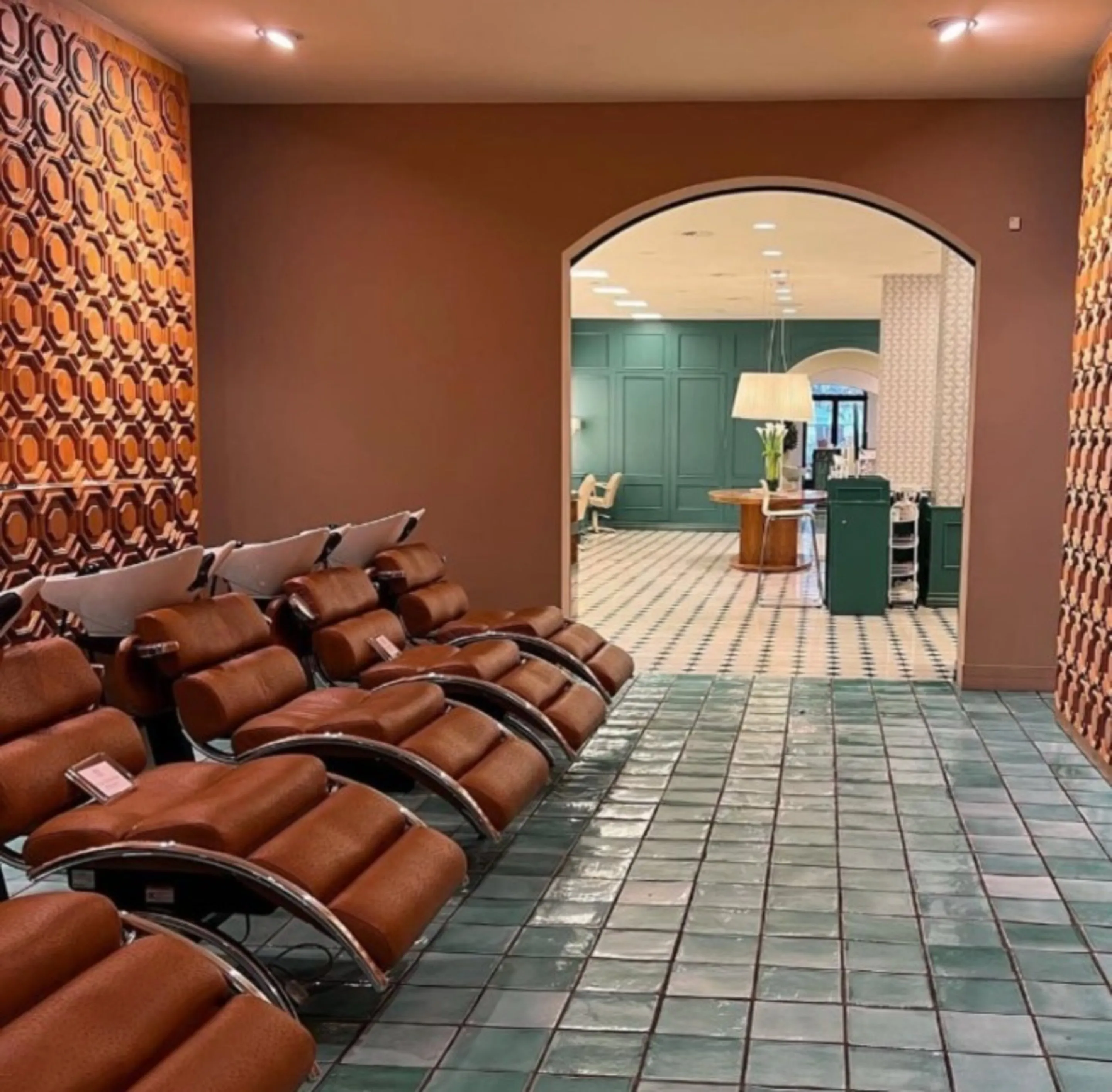 Waschbereich im Salon Georgstraße: cognacfarbene Lederliegen an einer Wand mit orangefarbenen Reliefkacheln, grüne Bodenfliesen und Rundbogen