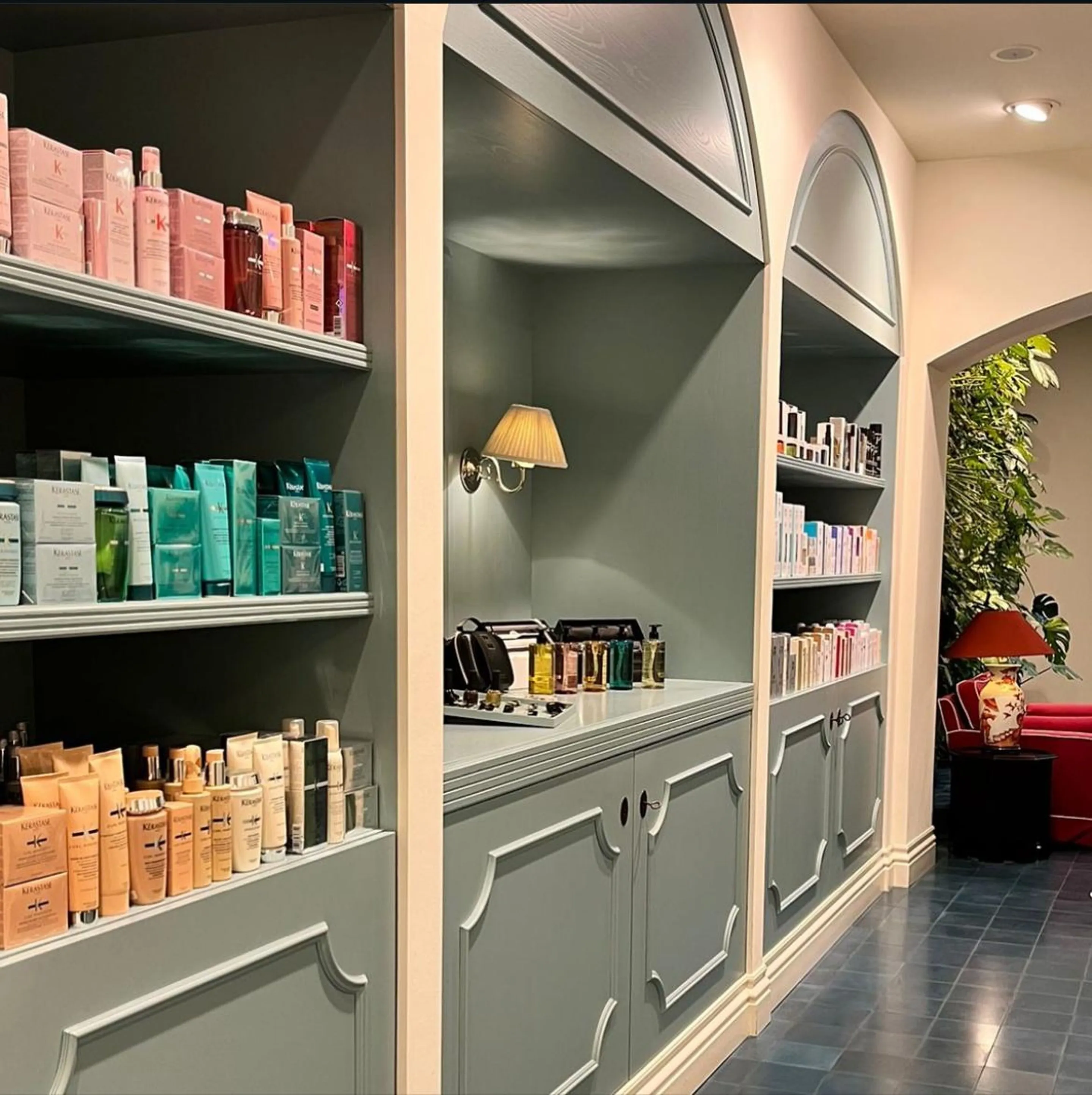 Produktregale im Salon Georgstraße: salbeigrüne Bogennischen mit farblich sortierten Haarpflegeprodukten, dahinter rote Sitzgruppe und Pflanzen