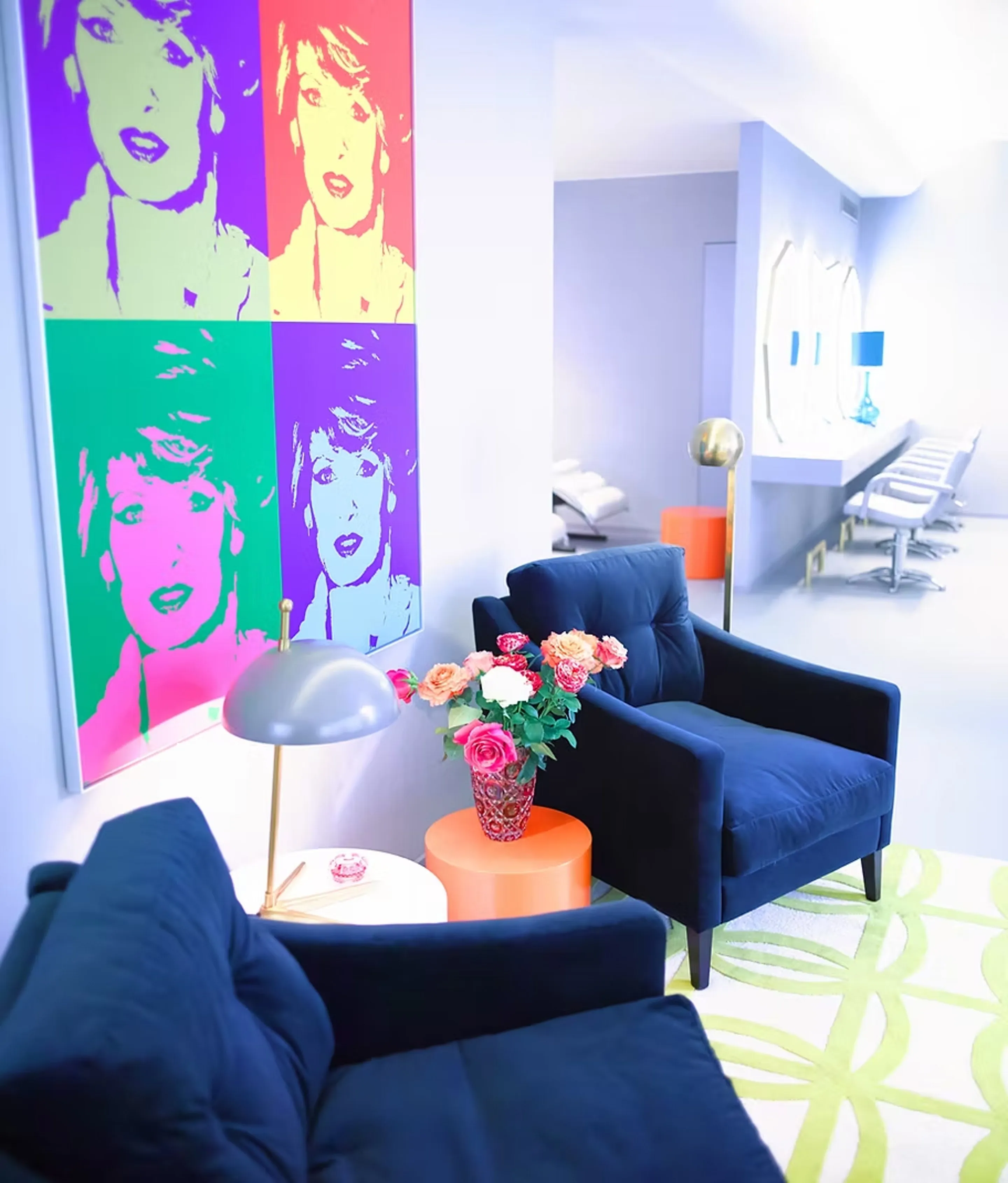 Wartebereich mit Pop-Art-Porträt in vier Farbfeldern, dunkelblauen Samtsesseln und orangefarbenen Beistelltischen