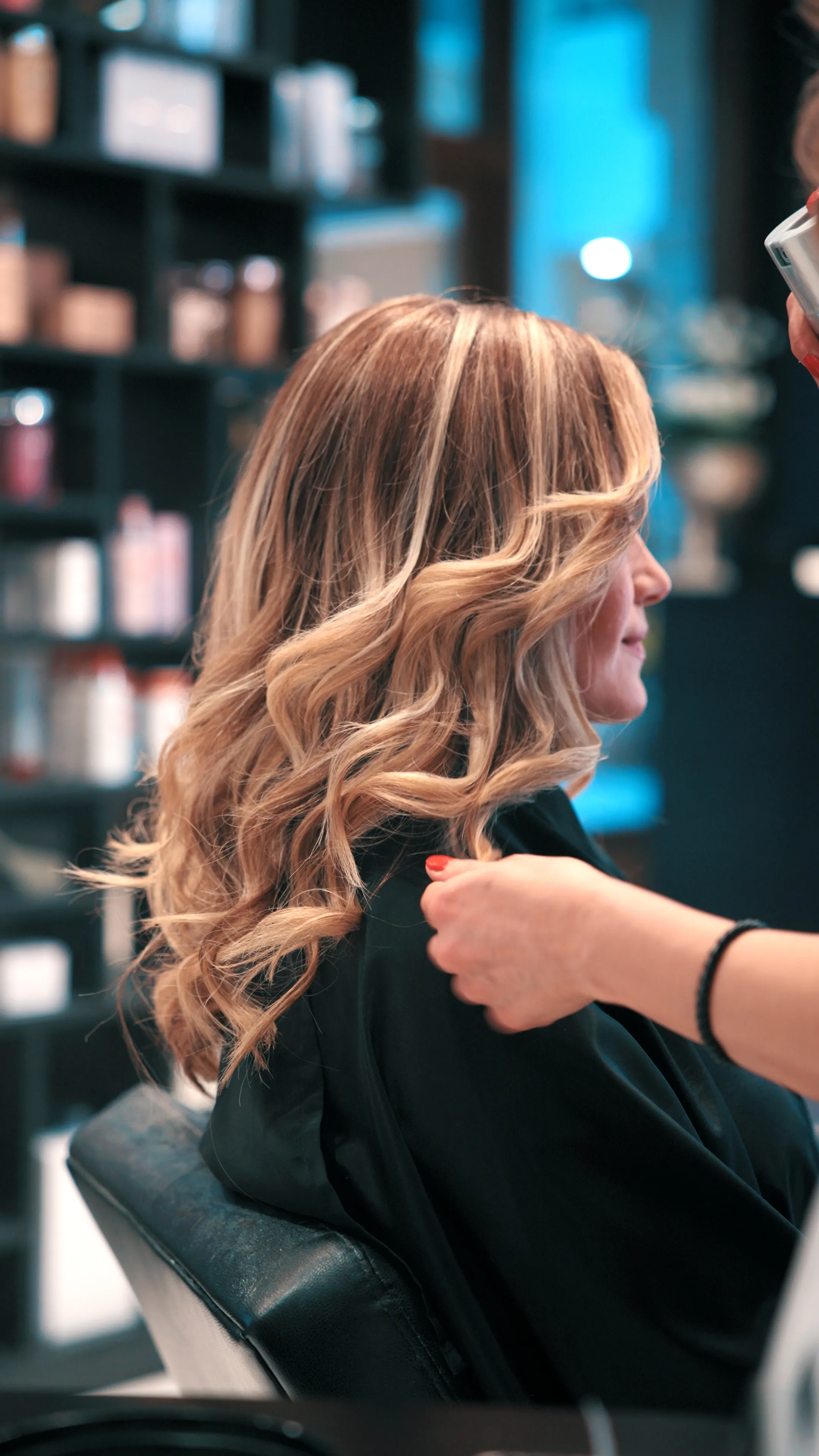Stylistin legt einer Kundin mit gewellten blonden Haaren im Salon den Umhang an